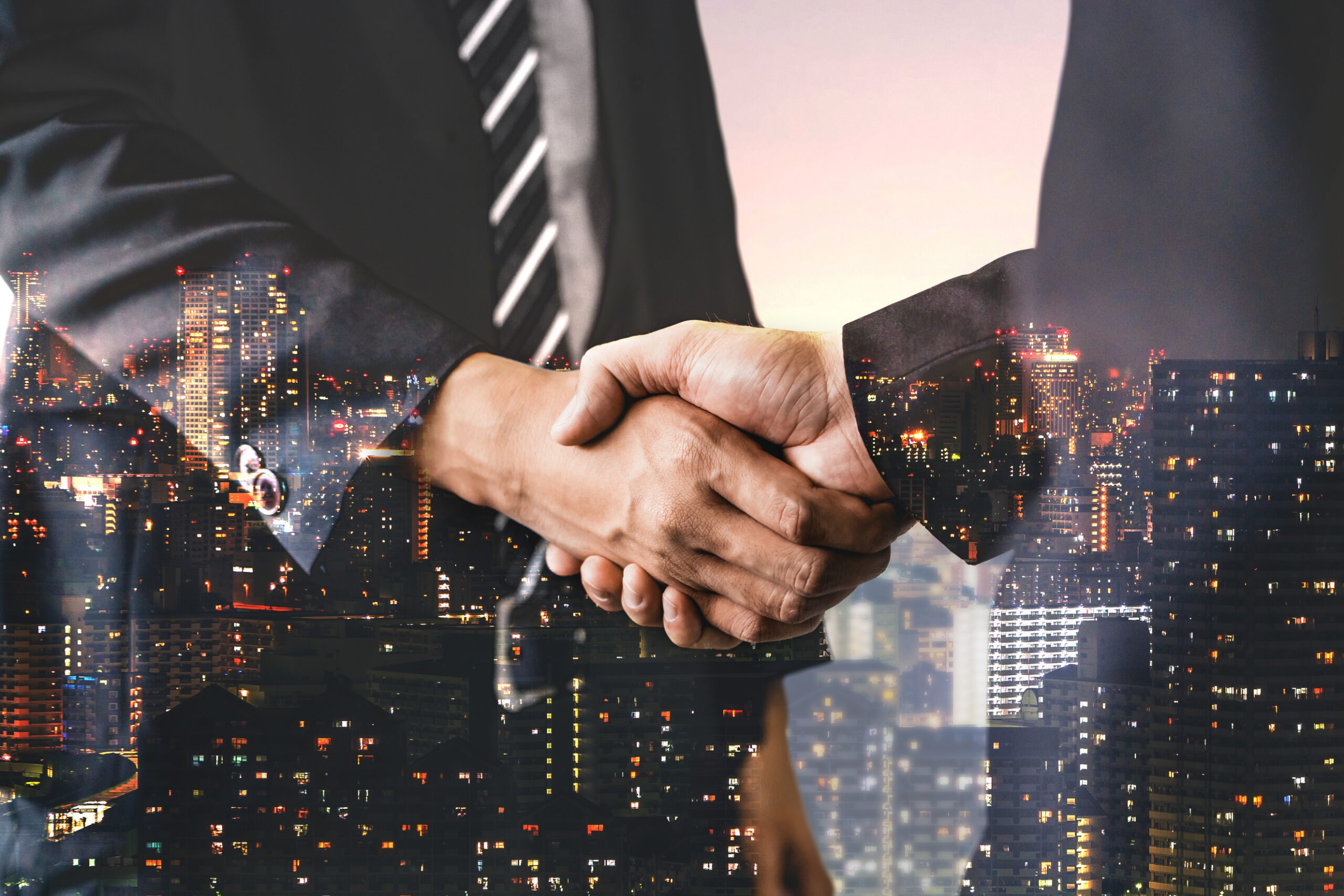 Business professionals shaking hands, set against a city skyline at dusk, symbolizing partnership and collaboration in a corporate environment.